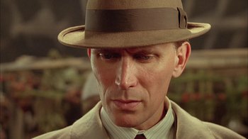 Movie still from “Naked Lunch” (1991), directed by David Cronenberg – A person wearing a suit and a hat; Close Up shot, Low angle