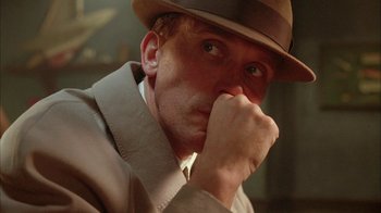Movie still from “Naked Lunch” (1991), directed by David Cronenberg – A person wearing a suit and a hat; Close Up shot, Low angle