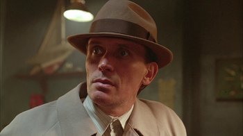Movie still from “Naked Lunch” (1991), directed by David Cronenberg – A person wearing a hat and a suit; Close Up shot, Low angle