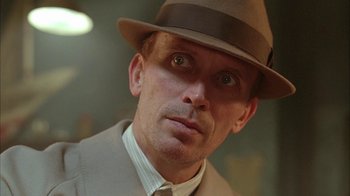 Movie still from “Naked Lunch” (1991), directed by David Cronenberg – A person wearing a suit and a hat; Close Up shot, Low angle