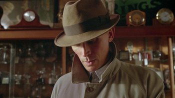 Movie still from “Naked Lunch” (1991), directed by David Cronenberg – A man wearing a hat and a jacket; Close Up shot, Low angle