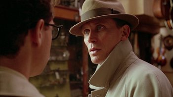 Movie still from “Naked Lunch” (1991), directed by David Cronenberg – A man wearing a hat and glasses talking to another man; Close Up shot, Over the shoulder angle