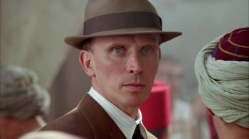 Movie still from “Naked Lunch” (1991), directed by David Cronenberg – A person wearing a suit and a hat; Close Up shot, Low angle