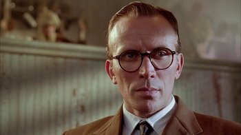 Movie still from “Naked Lunch” (1991), directed by David Cronenberg – A person wearing glasses and a suit; Close Up shot, Low angle