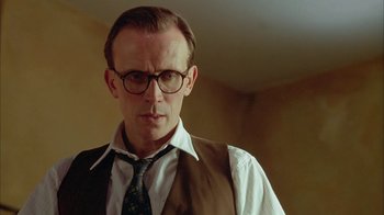 Movie still from “Naked Lunch” (1991), directed by David Cronenberg – A person wearing glasses and a tie; Close Up shot, Low angle