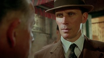 Movie still from “Naked Lunch” (1991), directed by David Cronenberg – A person wearing a suit and a hat; Close Up shot, Over the shoulder angle