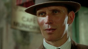Movie still from “Naked Lunch” (1991), directed by David Cronenberg – A person wearing a suit and a hat; Close Up shot, Low angle