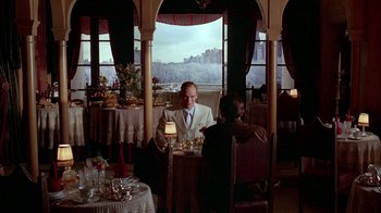 Movie still from “Naked Lunch” (1991), directed by David Cronenberg – A man and a woman sitting at a table in front of a window; Wide shot, Over the shoulder angle