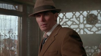 Movie still from “Naked Lunch” (1991), directed by David Cronenberg – A man in a suit and hat is standing in a room; Close Up shot, Low angle