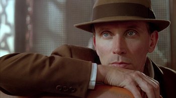 Movie still from “Naked Lunch” (1991), directed by David Cronenberg – A person wearing a suit and a hat; Close Up shot, Low angle