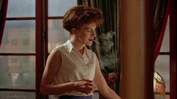 Movie still from “Naked Lunch” (1991), directed by David Cronenberg – A woman smoking a cigarette in front of a window; Medium shot, Low angle