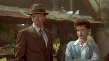 Movie still from “Naked Lunch” (1991), directed by David Cronenberg – A man and a woman standing next to each other in front of some birds; Medium shot, Low angle