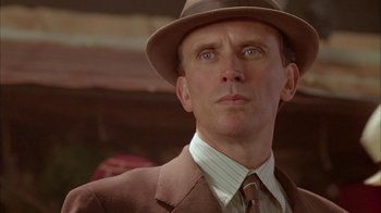 Movie still from “Naked Lunch” (1991), directed by David Cronenberg – A person wearing a suit and a hat; Close Up shot, Low angle