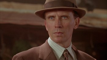 Movie still from “Naked Lunch” (1991), directed by David Cronenberg – A person wearing a suit and a hat; Close Up shot, Low angle