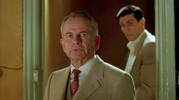 Movie still from “Naked Lunch” (1991), directed by David Cronenberg – A man in a suit and tie standing next to another man in a suit and tie; Medium shot, Low angle