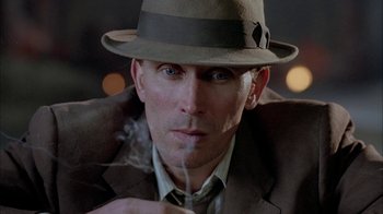 Movie still from “Naked Lunch” (1991), directed by David Cronenberg – A person wearing a hat and smoking a cigarette; Close Up shot, Low angle