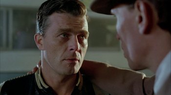 Movie still from “Naked Lunch” (1991), directed by David Cronenberg – A man is looking at another man in a hat; Close Up shot, Over the shoulder angle
