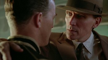 Movie still from “Naked Lunch” (1991), directed by David Cronenberg – A man in a suit and a hat talking to another man in a suit; Close Up shot, Over the shoulder angle
