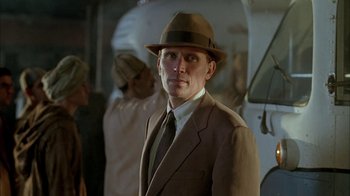 Movie still from “Naked Lunch” (1991), directed by David Cronenberg – A man in a suit and hat standing in front of a white van; Close Up shot, Low angle