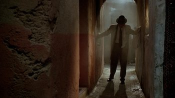Movie still from “Naked Lunch” (1991), directed by David Cronenberg – A man in a suit and tie standing in a hallway; Wide shot, Low angle
