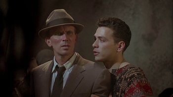 Movie still from “Naked Lunch” (1991), directed by David Cronenberg – A man in a suit and a hat standing next to a man in a suit; Close Up shot, Low angle