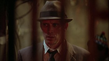 Movie still from “Naked Lunch” (1991), directed by David Cronenberg – A man wearing a hat and a suit and tie; Close Up shot, Low angle