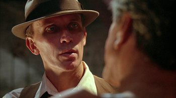 Movie still from “Naked Lunch” (1991), directed by David Cronenberg – A person wearing a hat; Close Up shot, Over the shoulder angle