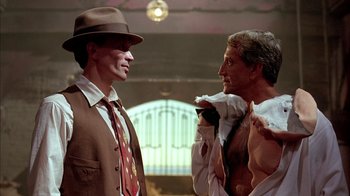 Movie still from “Naked Lunch” (1991), directed by David Cronenberg – A man in a suit and a hat standing next to another man in a suit; Medium shot, Low angle