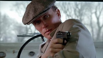 Movie still from “Naked Lunch” (1991), directed by David Cronenberg – A man holding a gun while sitting in a car; Close Up shot, Low angle
