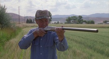 Movie still from “Napoleon Dynamite” (2004), directed by Jared Hess – An older man holding a rifle in a field; Medium shot, Over the shoulder angle