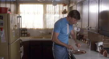 Movie still from “Napoleon Dynamite” (2004), directed by Jared Hess – A man standing in a kitchen preparing a pizza; Medium shot, Low angle