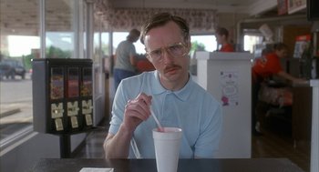 Movie still from “Napoleon Dynamite” (2004), directed by Jared Hess – A man sitting at a table with a drink in front of him; Close Up shot, Low angle