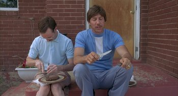Movie still from “Napoleon Dynamite” (2004), directed by Jared Hess – Two men sitting on the ground with plates of food; Medium shot, High angle