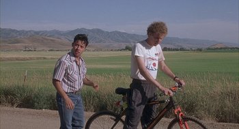 Movie still from “Napoleon Dynamite” (2004), directed by Jared Hess – Two men standing next to each other next to a bicycle; Wide shot, Low angle