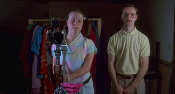 Movie still from “Napoleon Dynamite” (2004), directed by Jared Hess – A man and a woman standing next to each other in front of a camera; Medium shot, Low angle
