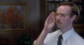 Movie still from “Napoleon Dynamite” (2004), directed by Jared Hess – A man in a white dress shirt and tie holding a pair of eyeglasses up to his face; Close Up shot, Low angle