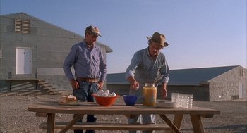 Movie still from “Napoleon Dynamite” (2004), directed by Jared Hess – A couple of men standing next to a wooden table; Medium shot, Low angle