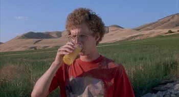 Movie still from “Napoleon Dynamite” (2004), directed by Jared Hess – A man drinking a glass of beer in a grassy field; Medium shot, High angle