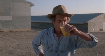 Movie still from “Napoleon Dynamite” (2004), directed by Jared Hess – An older man in a hat drinking a glass of orange juice; Medium shot, Low angle