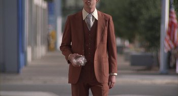 Movie still from “Napoleon Dynamite” (2004), directed by Jared Hess – A man in a suit and tie holding a sandwich; Medium shot, Low angle