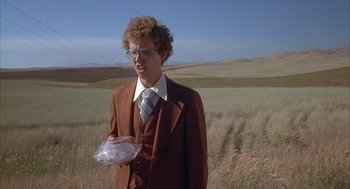 Movie still from “Napoleon Dynamite” (2004), directed by Jared Hess – A man in a brown suit holding a plastic bag in a field; Medium shot, Low angle