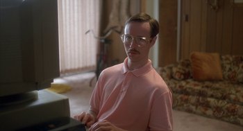 Movie still from “Napoleon Dynamite” (2004), directed by Jared Hess – A man in a pink shirt is typing on a laptop computer; Medium shot, High angle