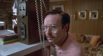 Movie still from “Napoleon Dynamite” (2004), directed by Jared Hess – A man wearing glasses and a pink shirt is looking at a phone; Close Up shot, Low angle