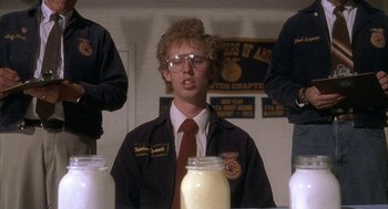 Movie still from “Napoleon Dynamite” (2004), directed by Jared Hess – A man in a uniform sitting in front of jars of milk; Medium shot, Over the shoulder angle