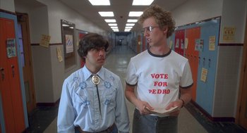 Movie still from “Napoleon Dynamite” (2004), directed by Jared Hess – Two men standing in a hallway with a vote for pedro t - shirt on; Medium shot, Overhead angle