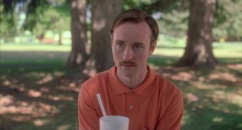 Movie still from “Napoleon Dynamite” (2004), directed by Jared Hess – A man in a red shirt is holding a drink; Close Up shot, Low angle