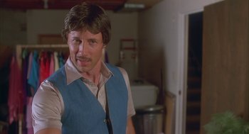 Movie still from “Napoleon Dynamite” (2004), directed by Jared Hess – A man in a blue vest standing in a room; Close Up shot, Over the shoulder angle