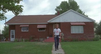 Movie still from “Napoleon Dynamite” (2004), directed by Jared Hess – A man standing in front of a house holding a frisbee; Wide shot, Low angle