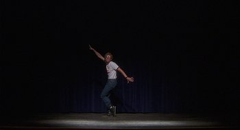 Movie still from “Napoleon Dynamite” (2004), directed by Jared Hess – A man on a stage doing a trick on a skateboard; Wide shot, Low angle