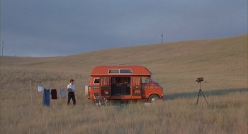 Movie still from “Napoleon Dynamite” (2004), directed by Jared Hess – A man standing next to an orange van in a grassy field; Extreme Wide shot, Low angle